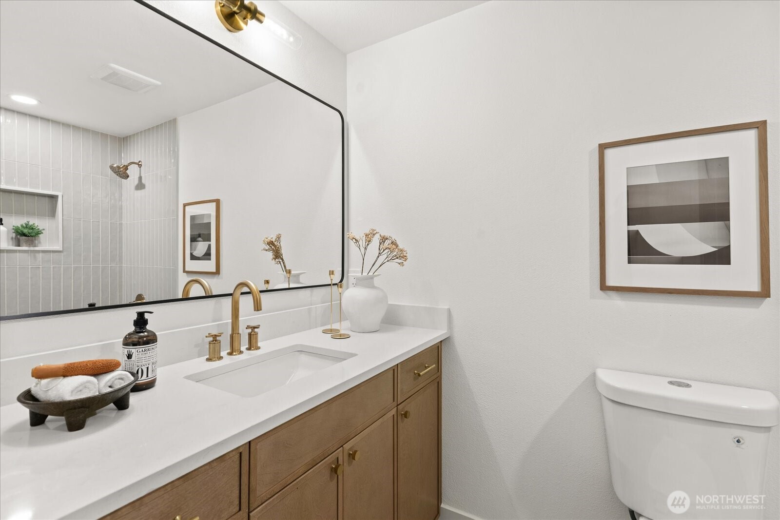 Bathroom vanity with a white countertop, wood cabinetry, brass fixtures, and a large mirror.