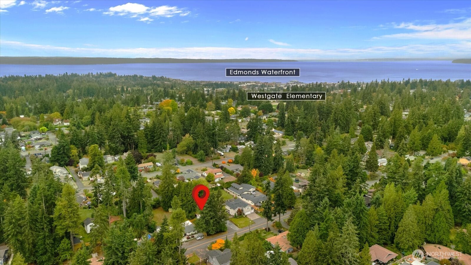 Aerial view of a wooded neighborhood, with a red pin marking the property and water visible beyond.