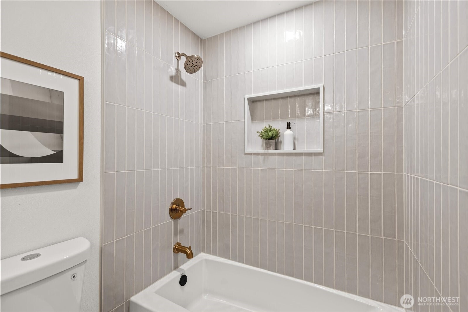 Bathroom tub and shower with pale vertical tile, brass fixtures, and a recessed display niche.