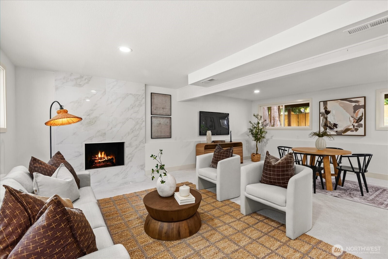 Staged living room with a lit fireplace, white seating, and an adjoining dining area.