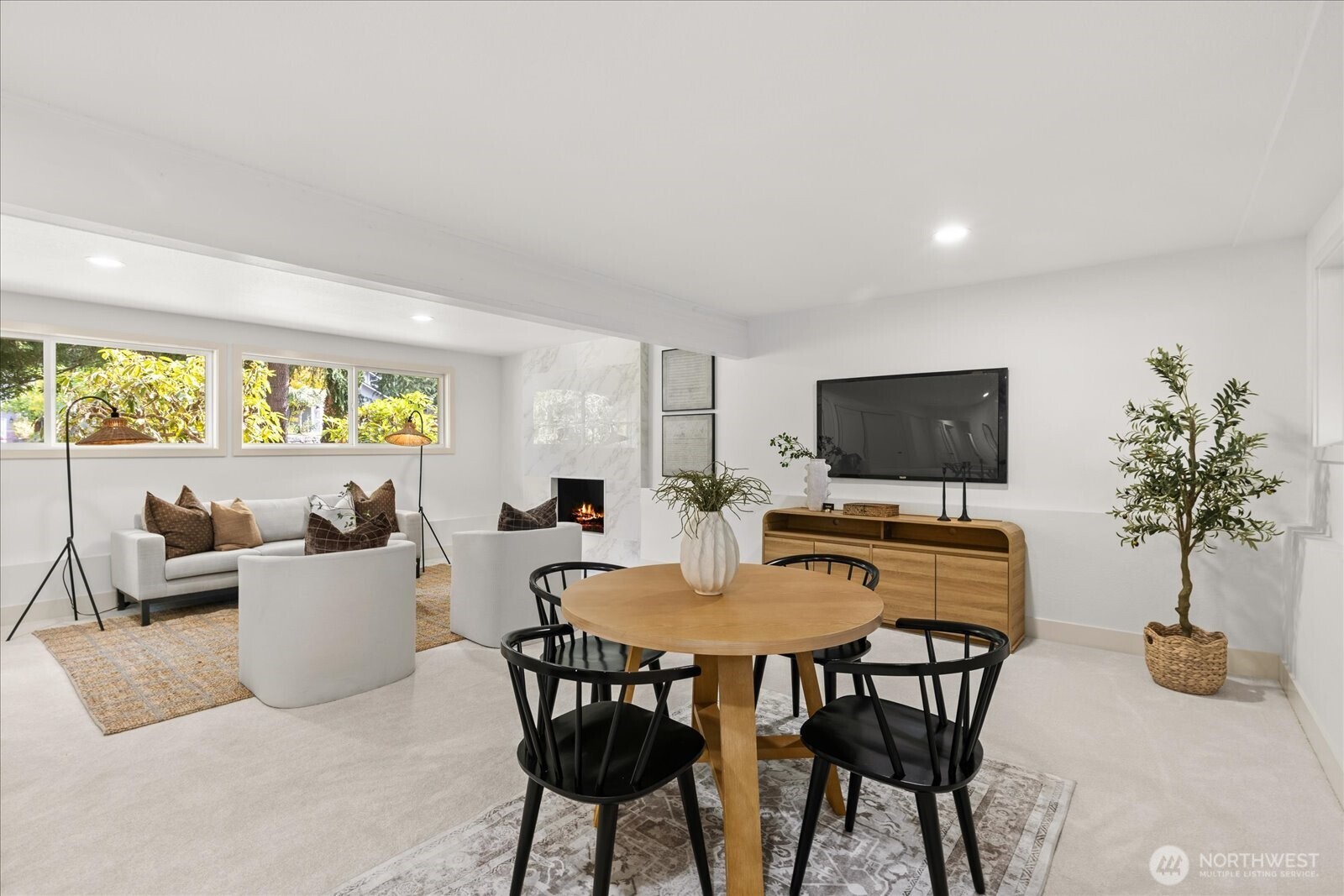 Staged living and dining room with a round wood table, white seating, and a marble-surround fireplace.