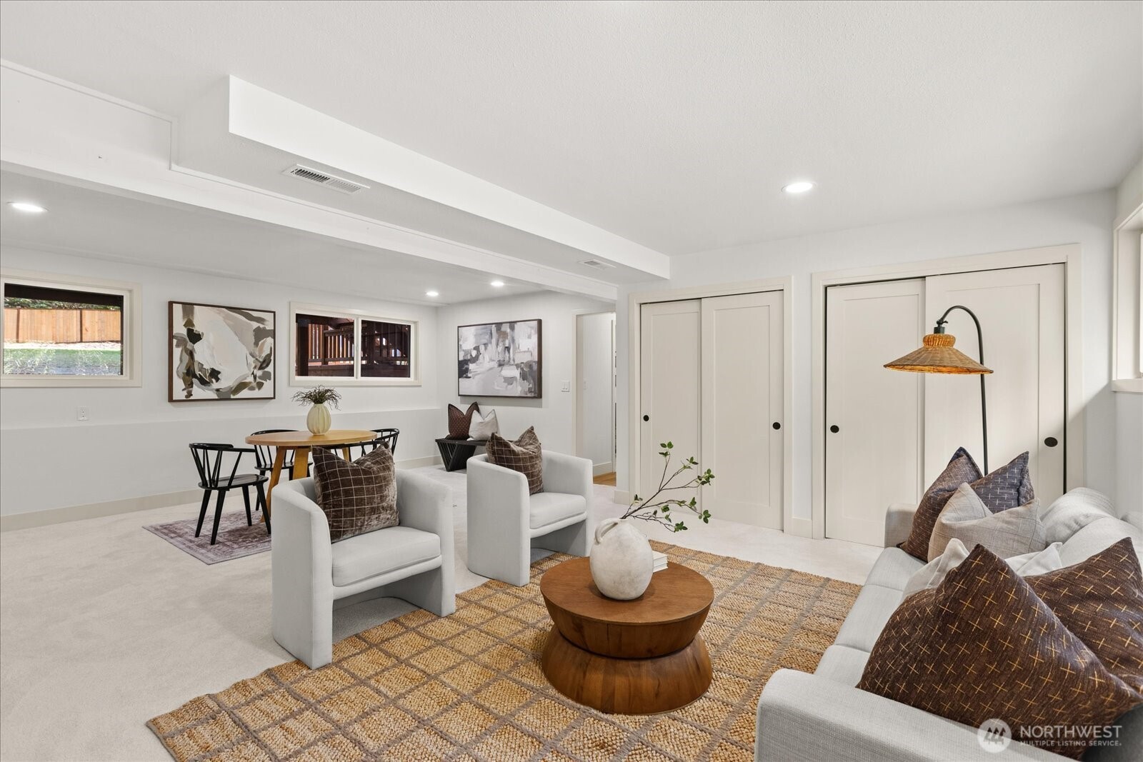 Staged living and dining area with white sofas, a round wooden coffee table, and patterned rugs.