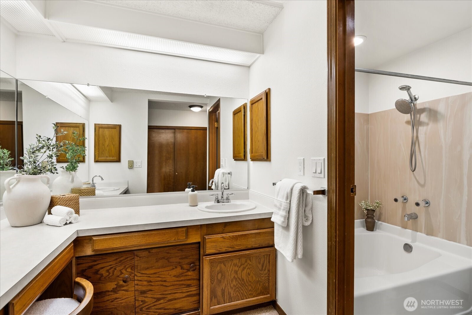 Bathroom with a wood vanity and large mirror beside a bathtub and shower.
