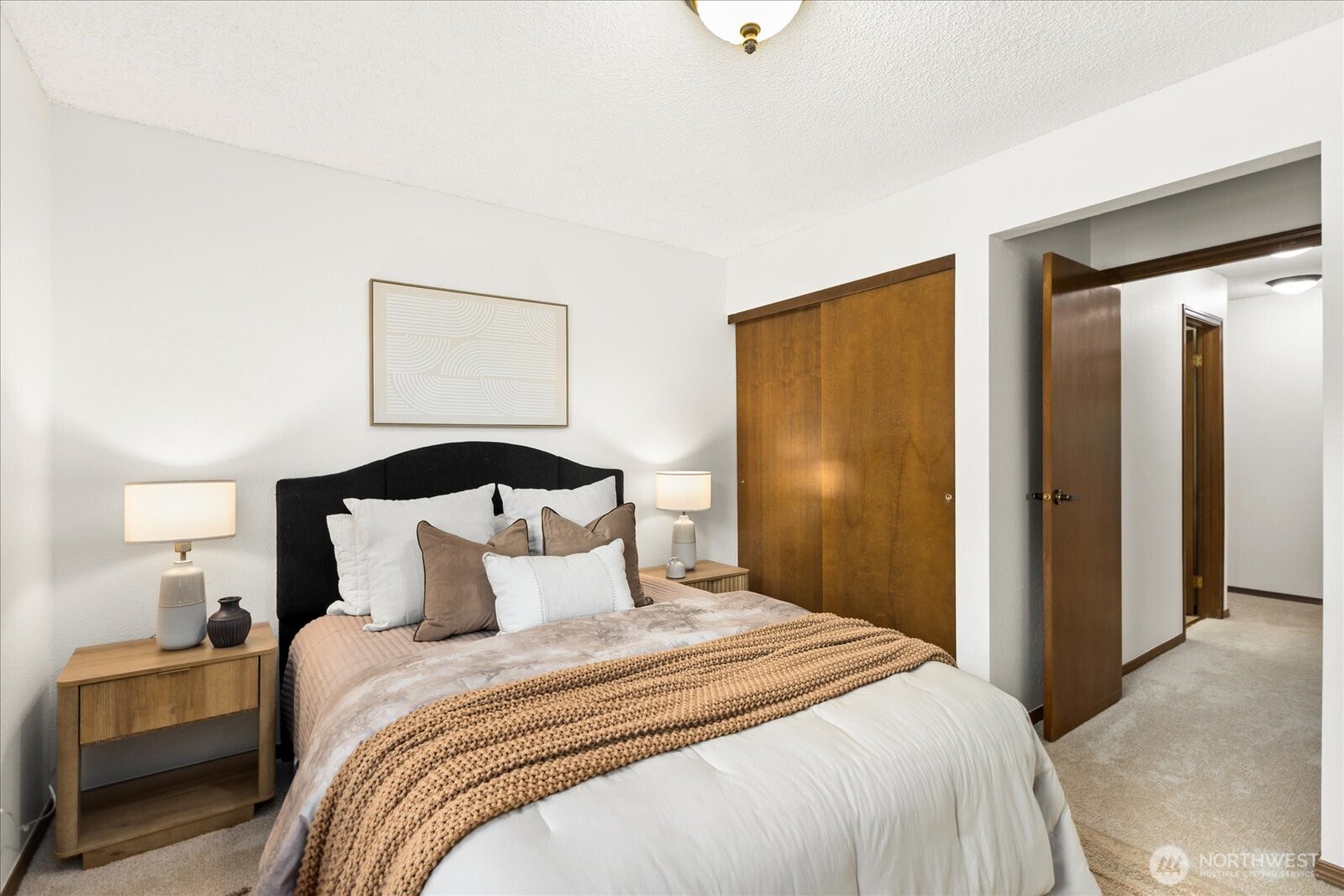 Staged bedroom with a black headboard, wooden bedside tables, and sliding wooden closet doors.