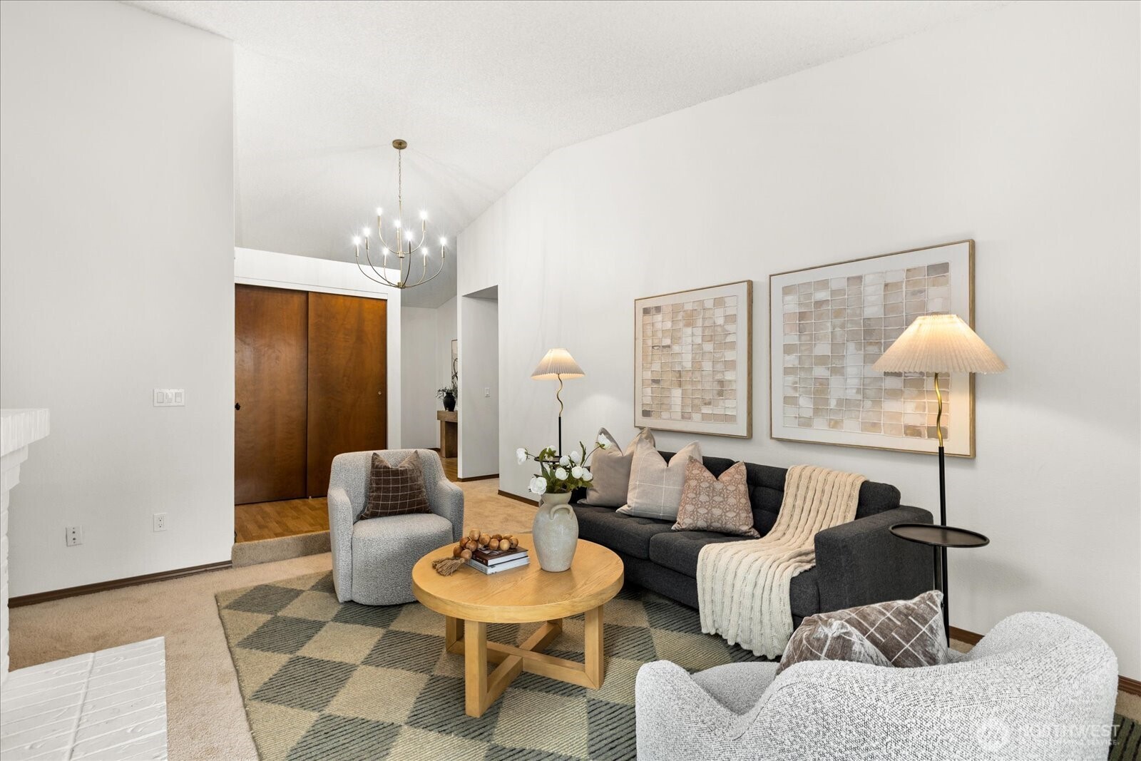 Staged living room with a vaulted ceiling, chandelier, dark sofa, and round wood coffee table.