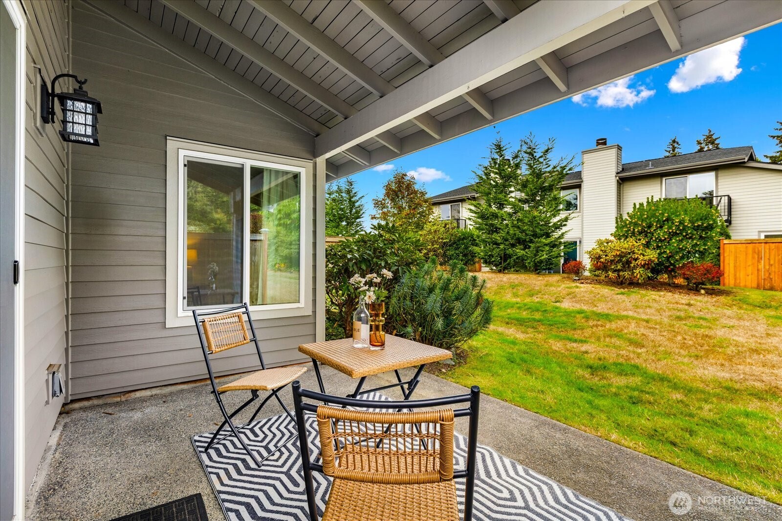 Covered patio with woven seating and a small table overlooking a landscaped lawn.