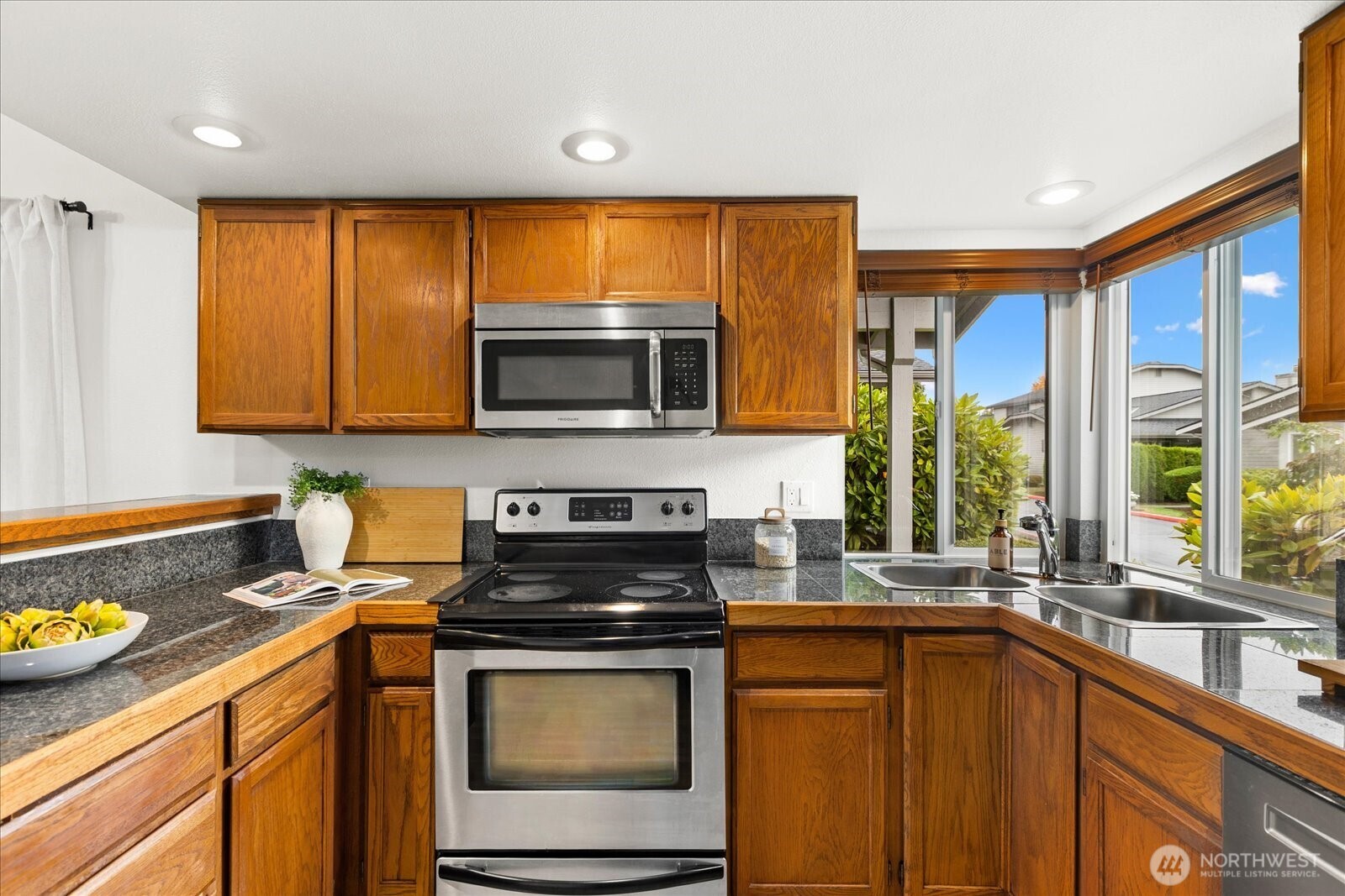 Kitchen with honey-toned wood cabinets, granite counters, stainless appliances, and a window-side sink.
