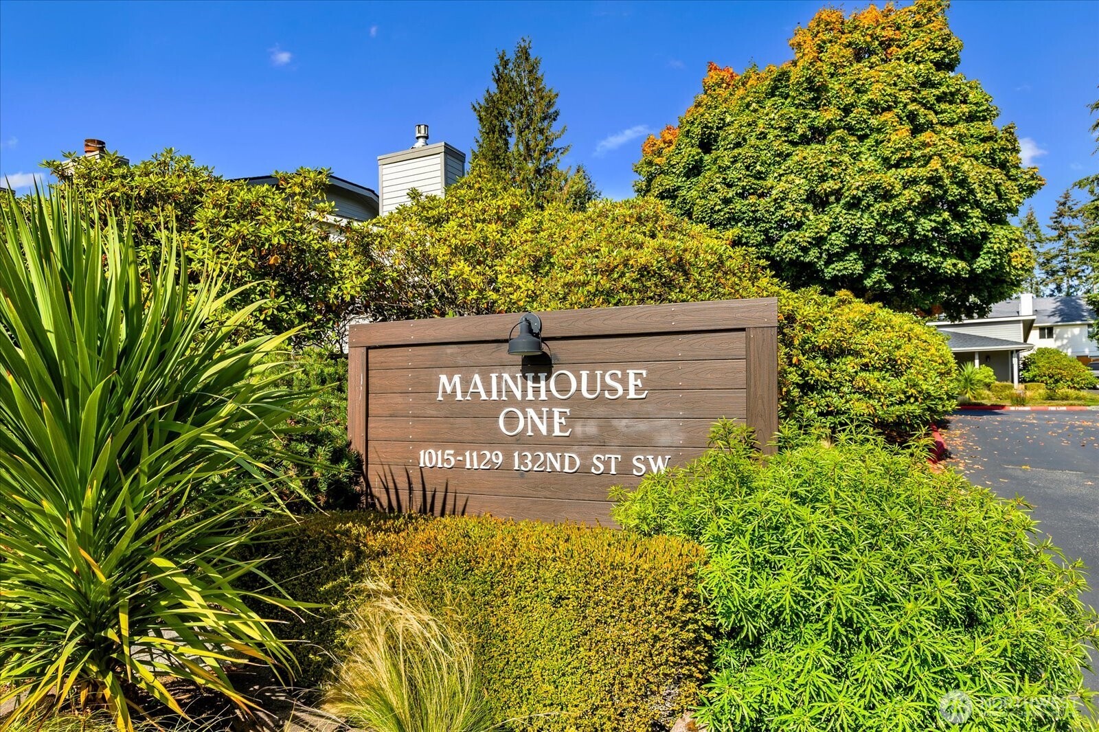Mainhouse One entrance sign among landscaped shrubs and autumn-colored trees.