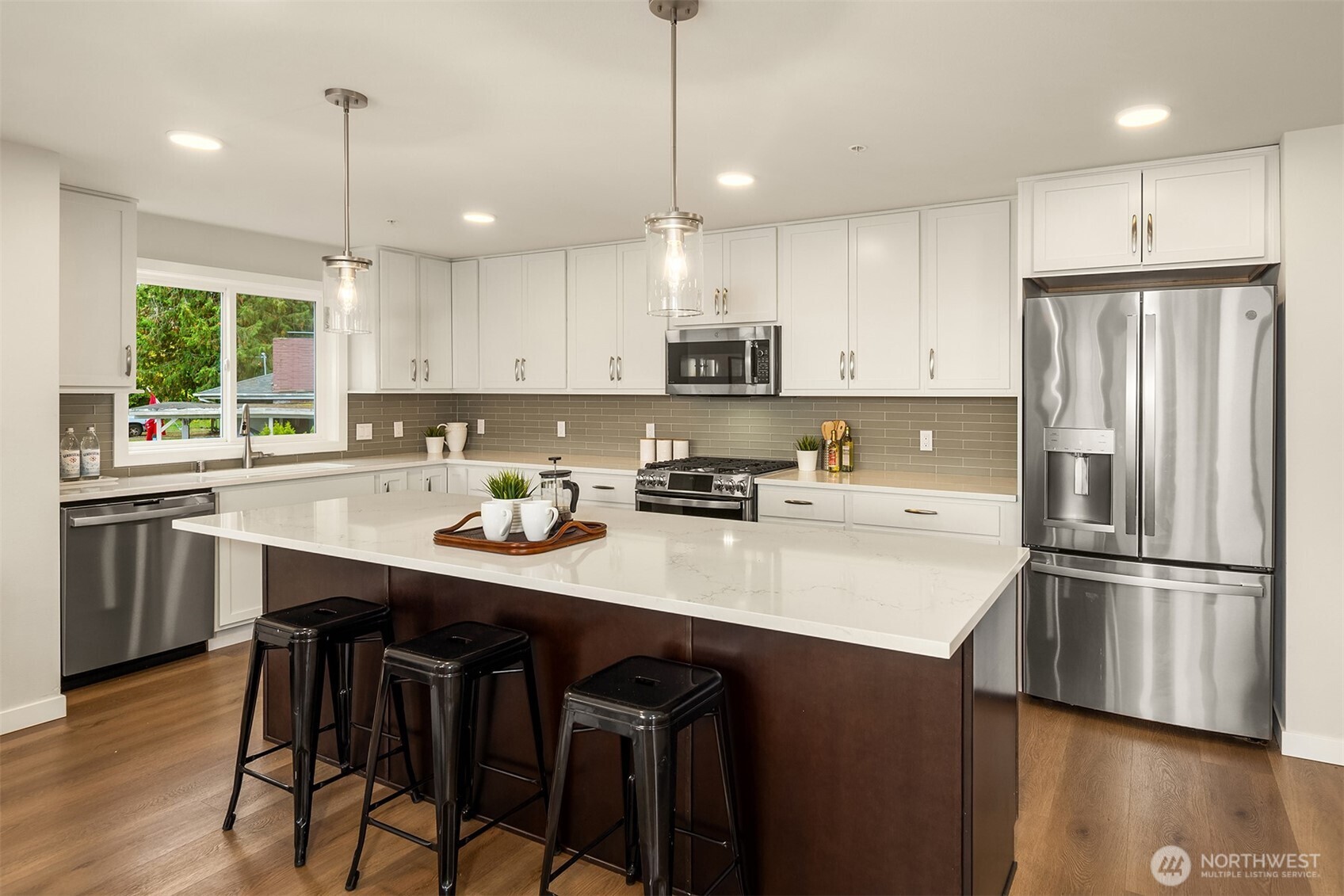 Kitchen with a large island, three black stools, white cabinets, and stainless steel appliances.
