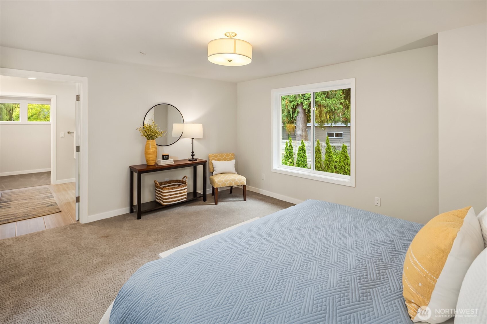 Staged bedroom with a blue quilted bed and a large window overlooking greenery.