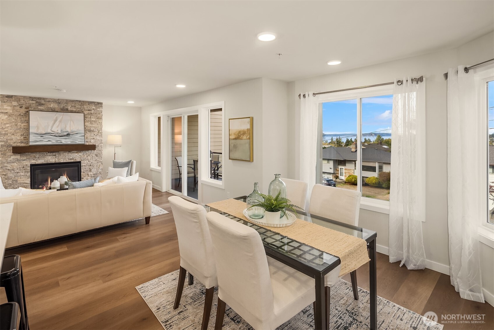 Open-plan living and dining area with a stone fireplace and water visible through the windows.