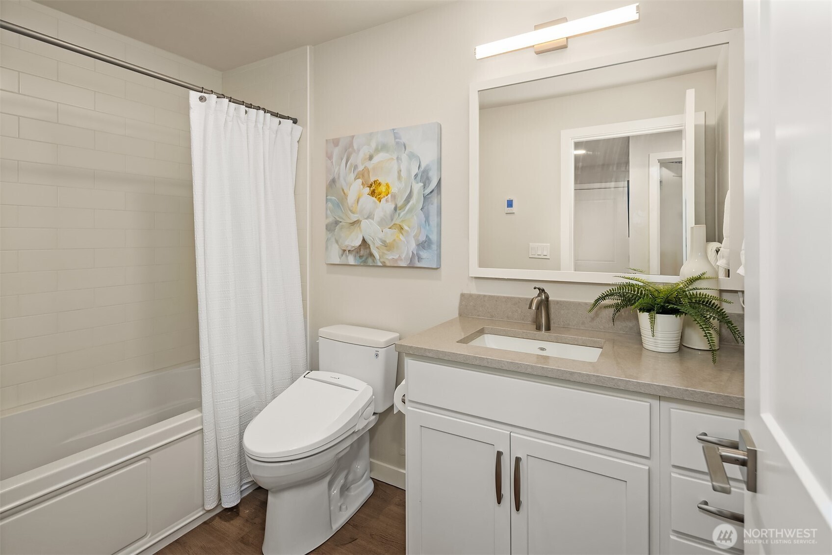 Bathroom with a white vanity and fern beside a tub with a white shower curtain.