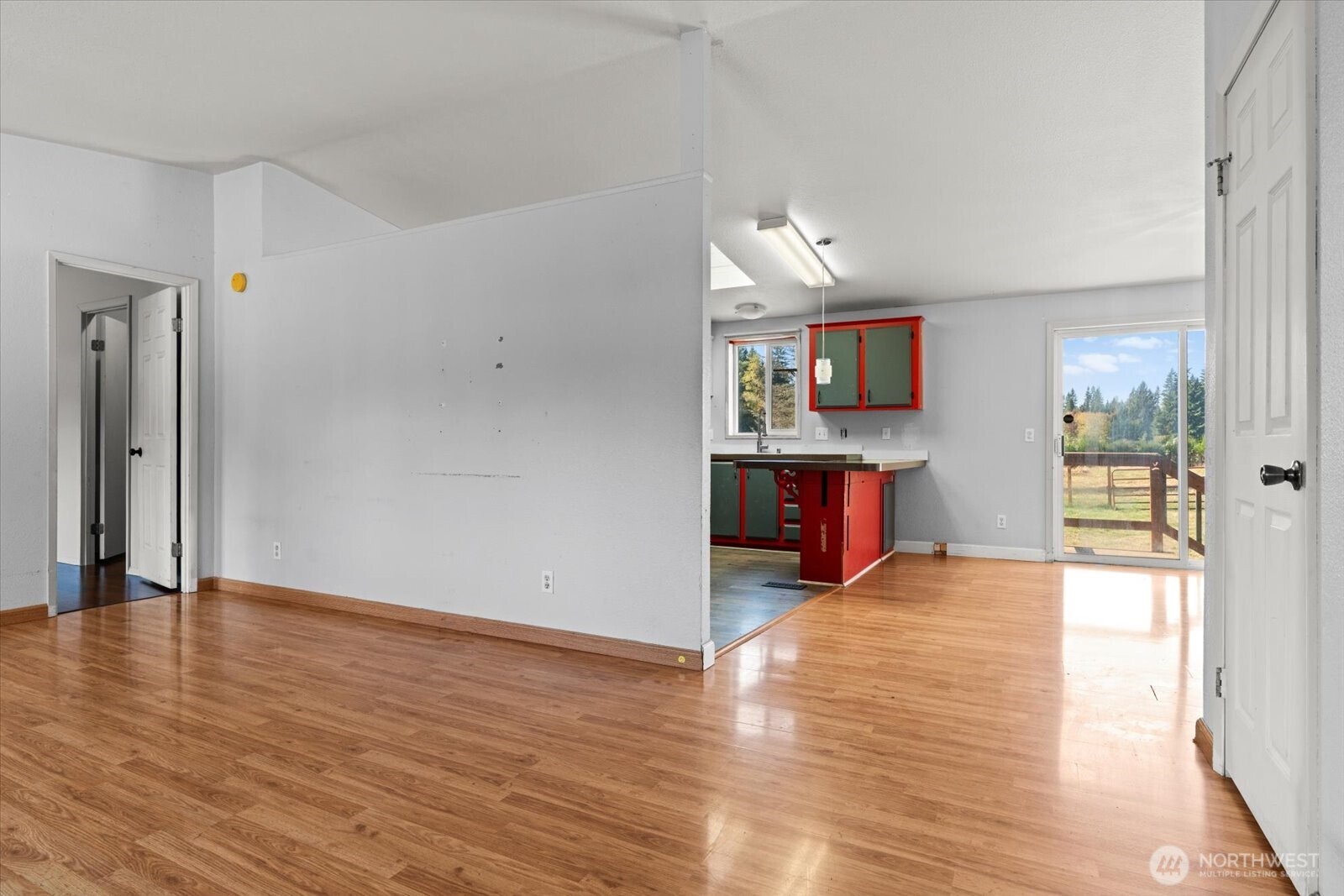 Unfurnished living area and kitchen with red and green cabinets, wood-look floors, and a sliding door to the yard.
