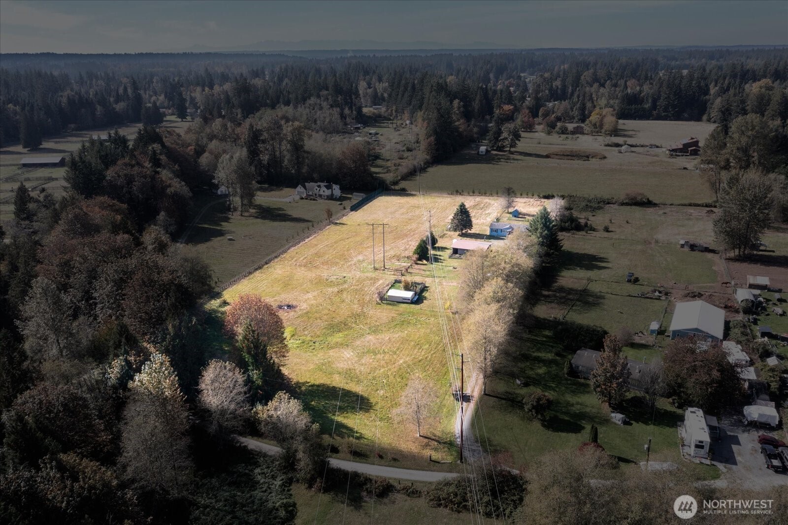 Aerial view of a grassy rural property bordered by trees, with utility lines crossing the open field.
