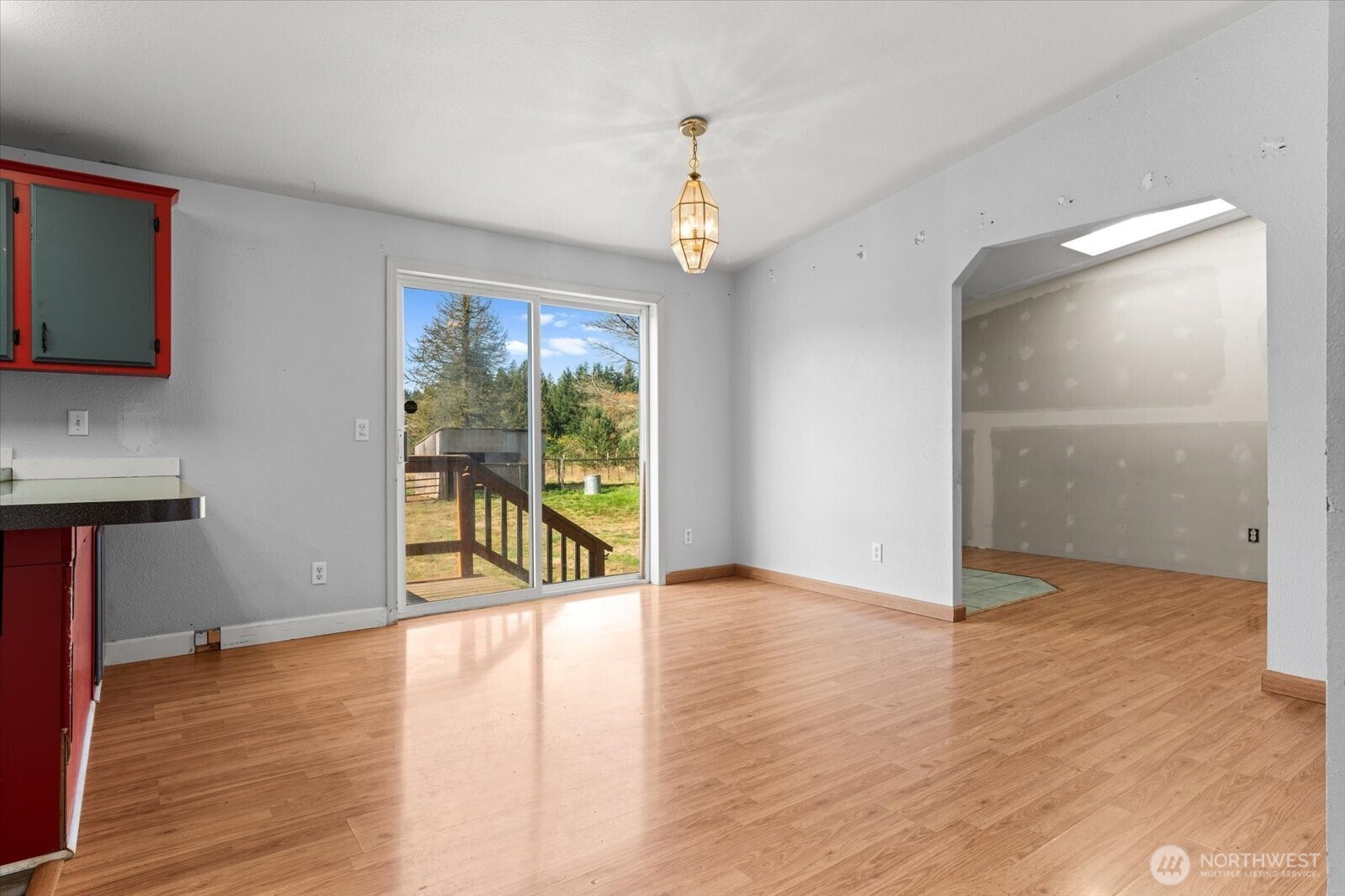 Vacant kitchen and dining area with red cabinets, wood-look flooring, and a sliding door to the yard.