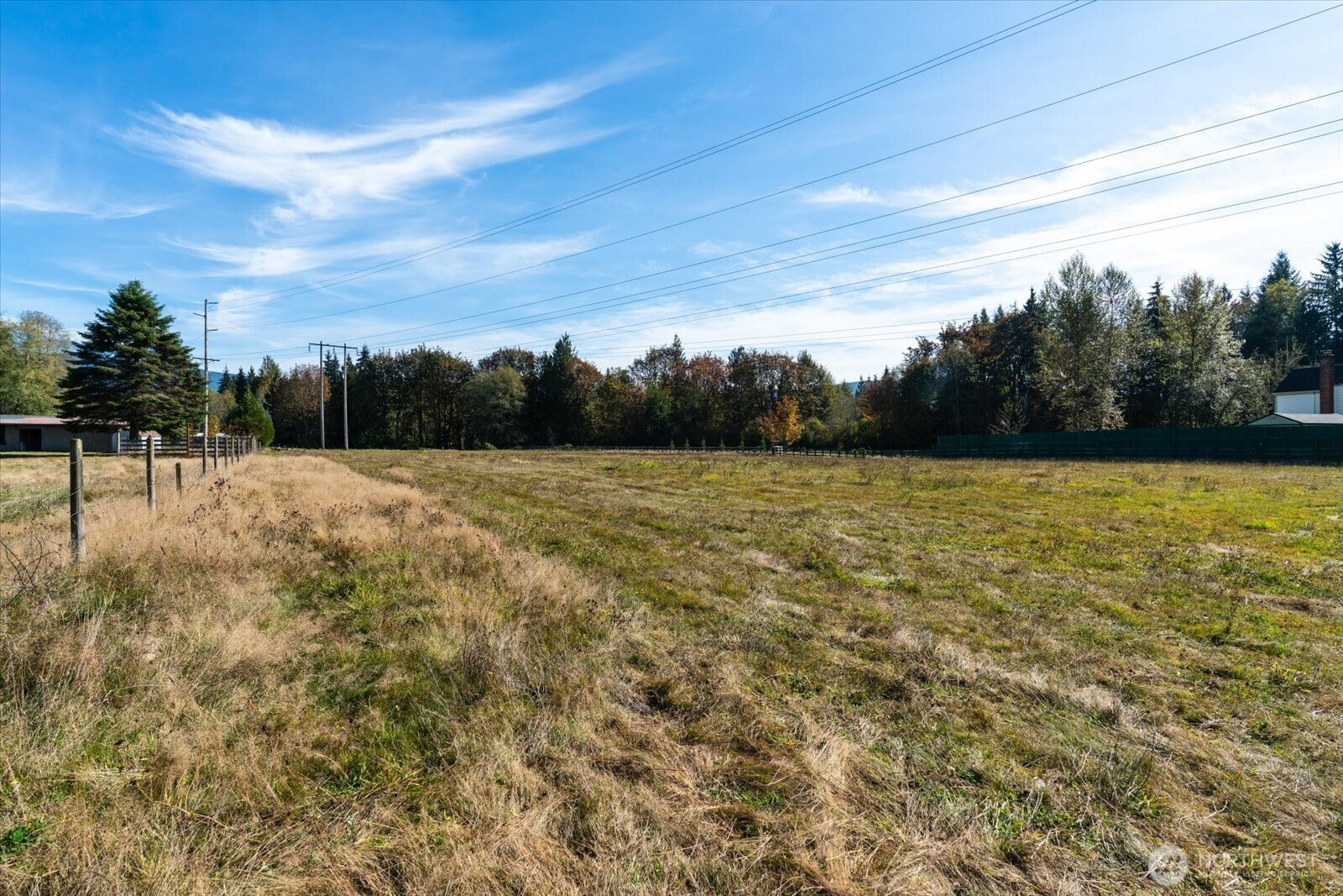 Open grassy parcel with fence lines, mature trees, and utility wires overhead.