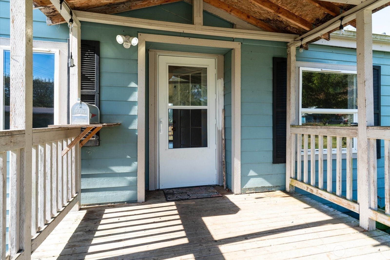 Covered wooden porch with white railings and a screened door on a blue house.