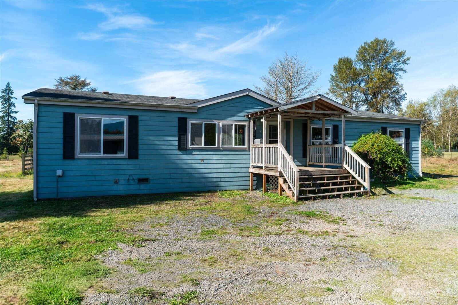 Blue single-story home with a covered wooden porch and gravel driveway.
