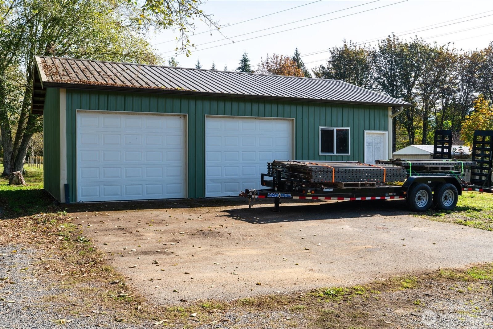 Green detached garage with two white overhead doors and a loaded utility trailer parked in front.