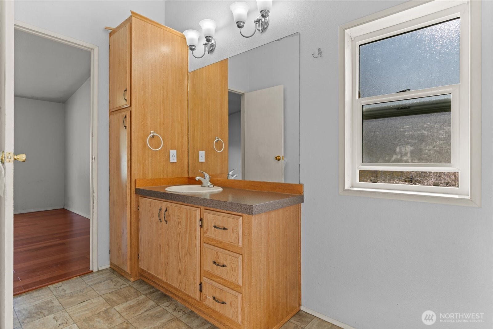 Bathroom vanity with light wood cabinets, a large mirror, and a window.