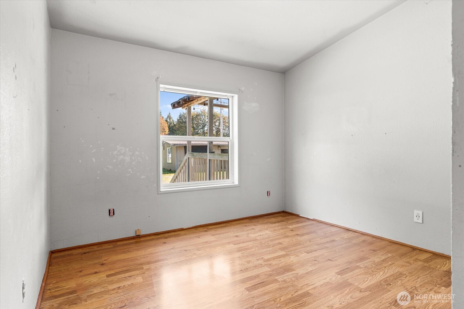 Empty room with hardwood floors, white walls, and a window overlooking a wooden deck.