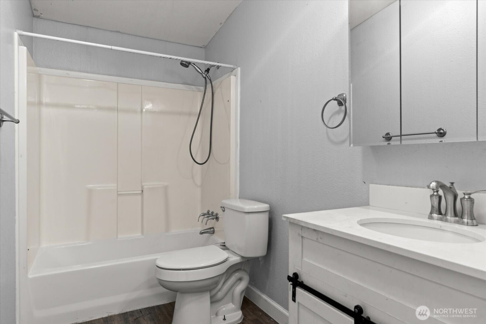 Bathroom with a white tub and shower, toilet, and vanity with mirrored cabinet.