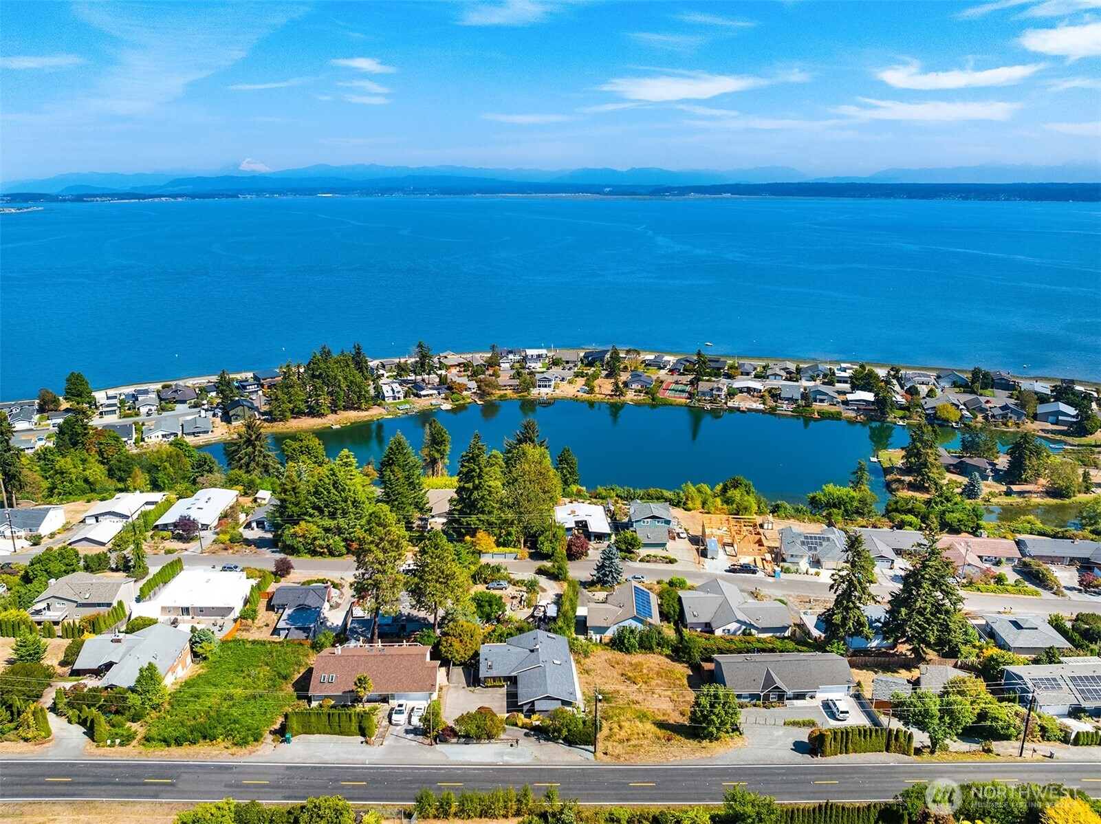 Aerial view of homes around a small lake, with Puget Sound and distant mountains beyond.