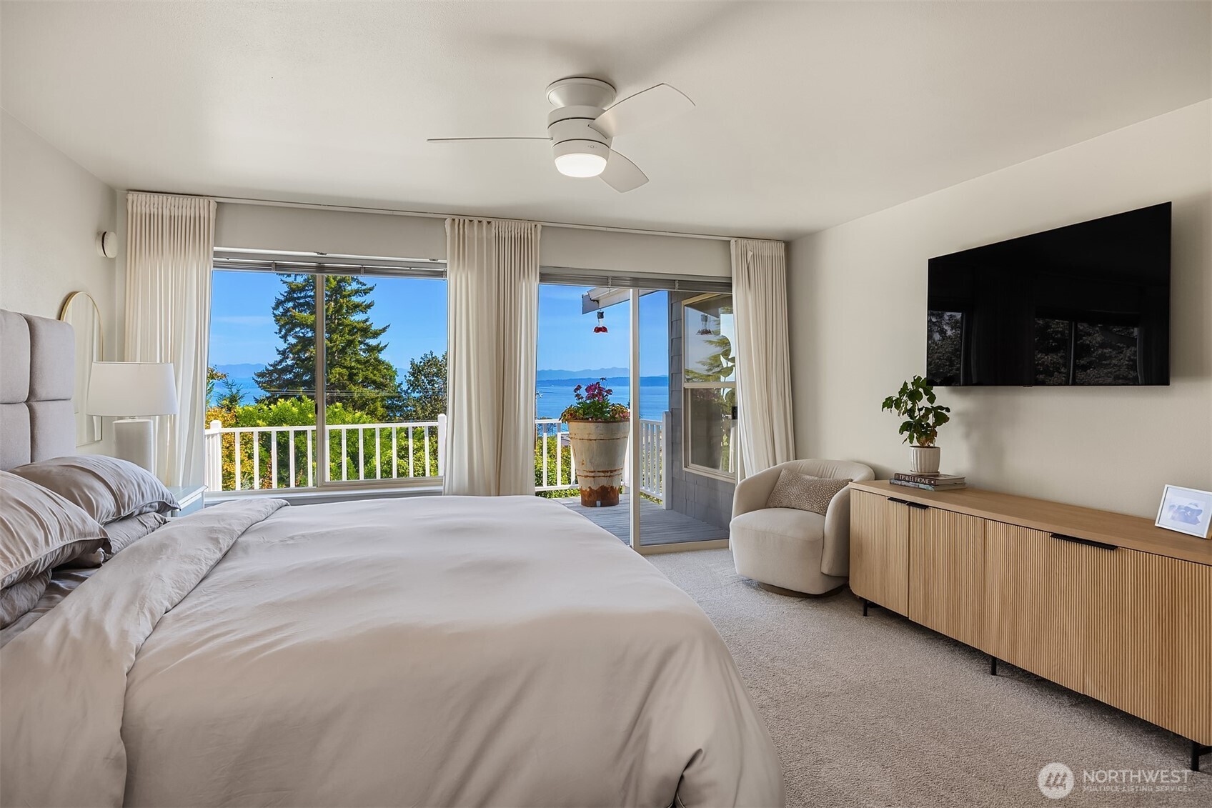 Bedroom with balcony doors overlooking water and distant mountains.