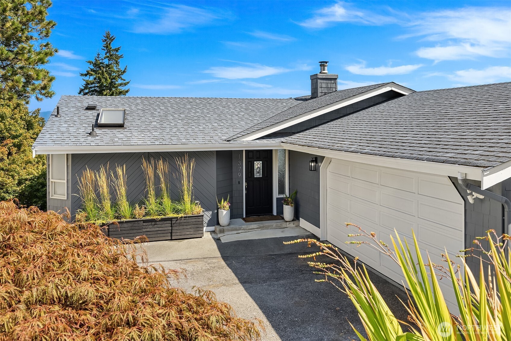 Gray house with a white garage door, black entry, and landscaped planters beside the driveway.