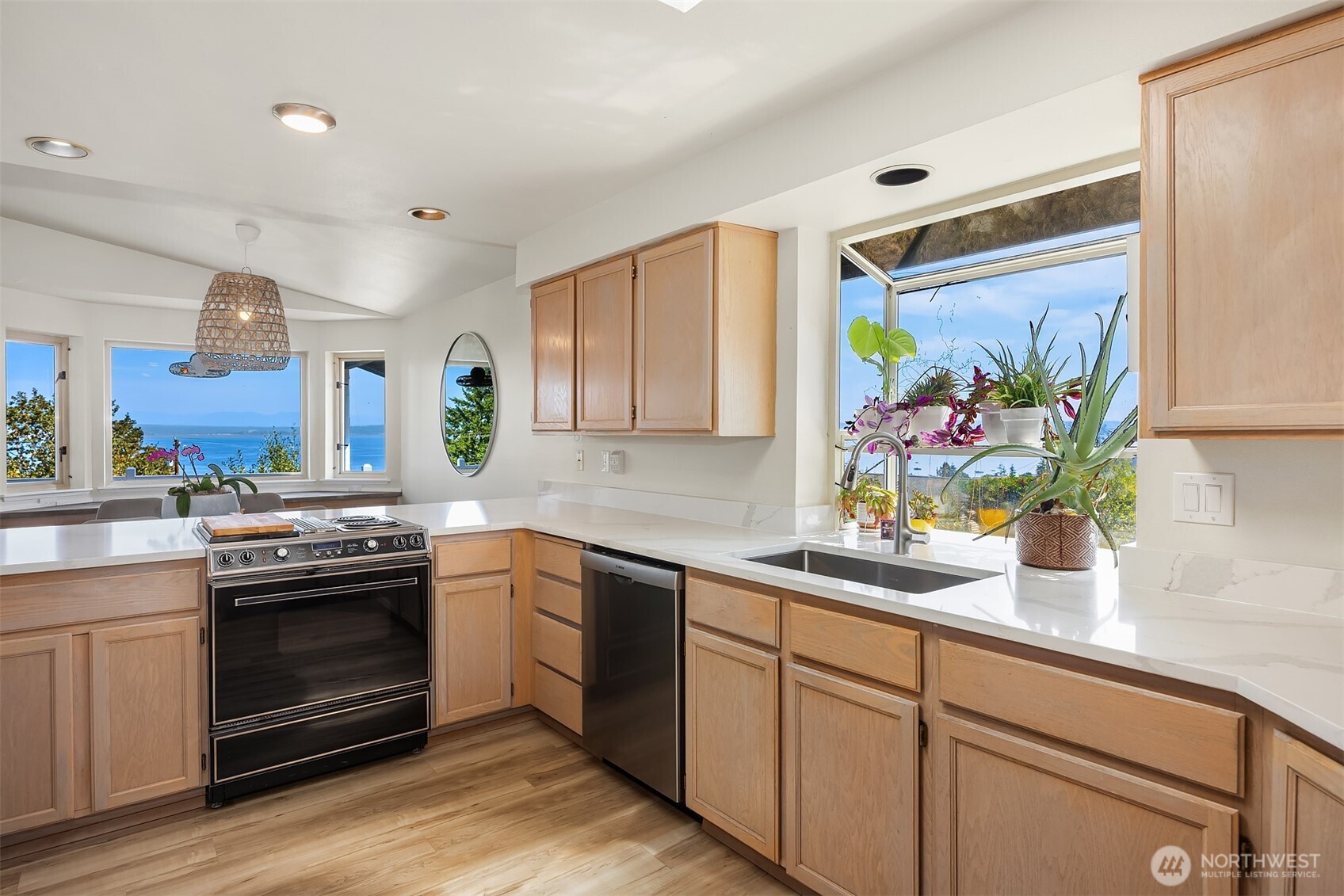 Bright kitchen with light wood cabinetry, white counters, and water views through large windows.