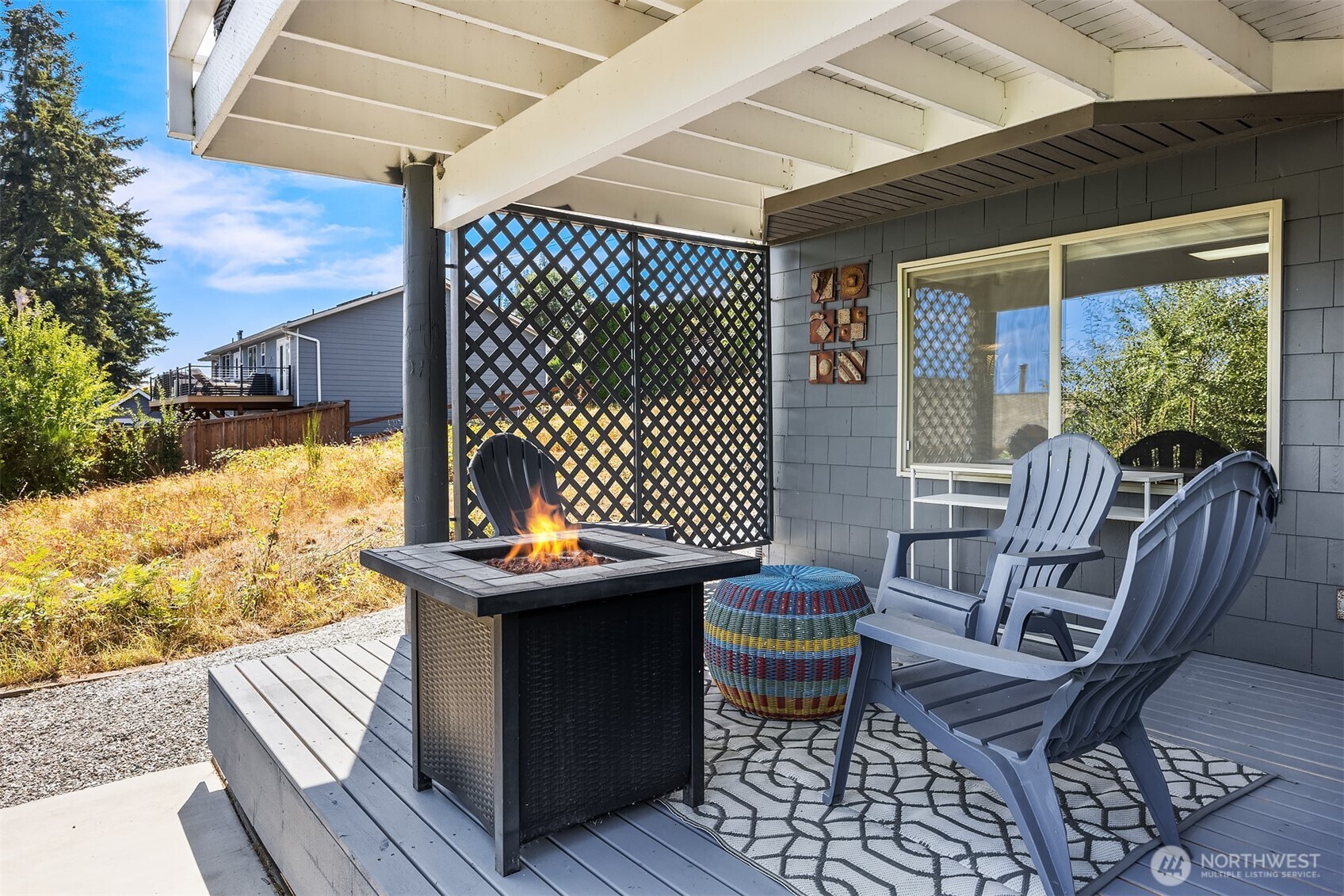 Covered patio with a fire table, Adirondack chairs, and lattice privacy screen.