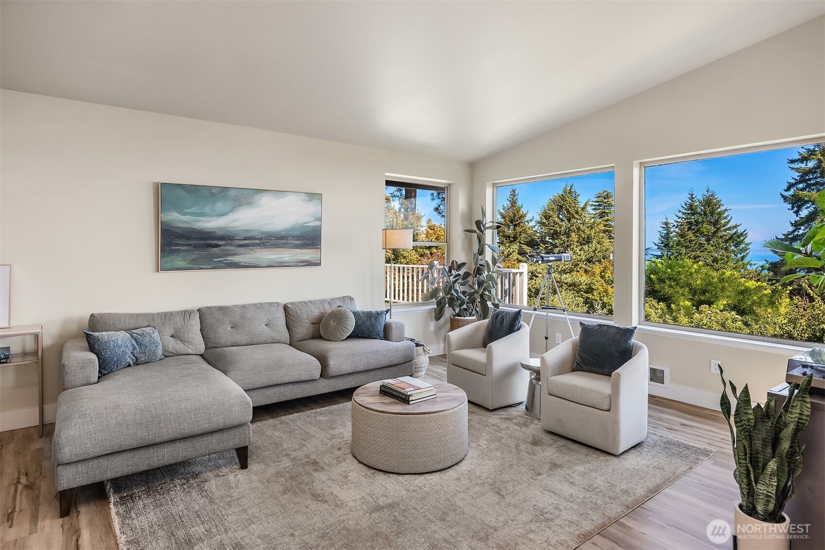 Staged living room with a gray sectional and large windows overlooking trees and water.