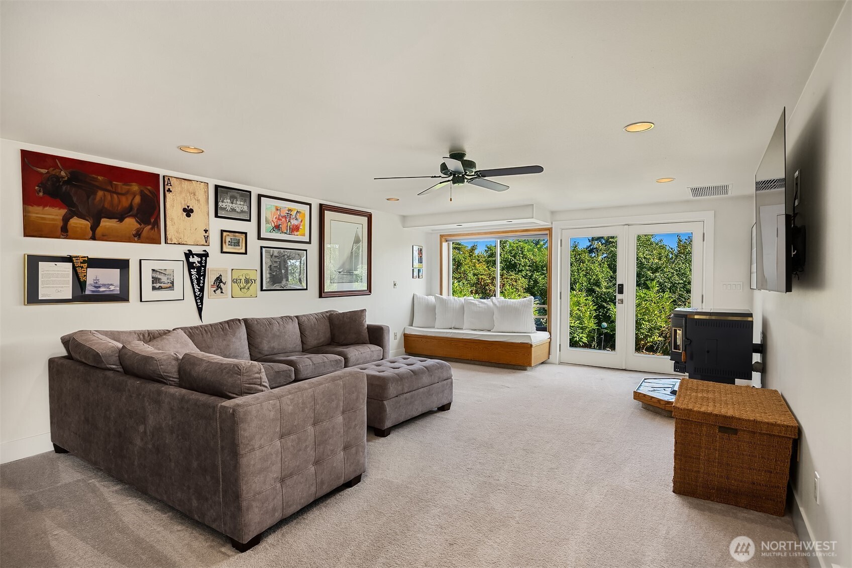 Living room with a gray sectional, gallery wall, window seat, and glass doors facing greenery.