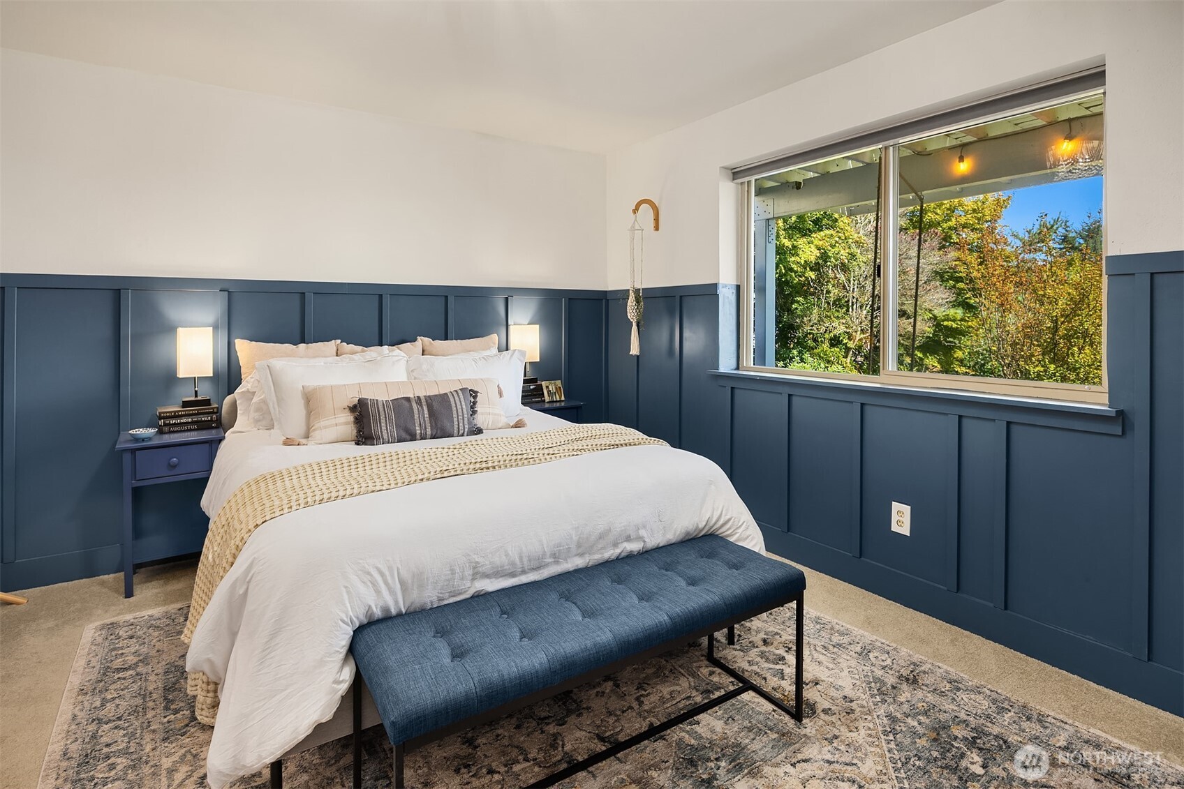 Bedroom with navy paneled walls, a white bed, and a large window overlooking trees.