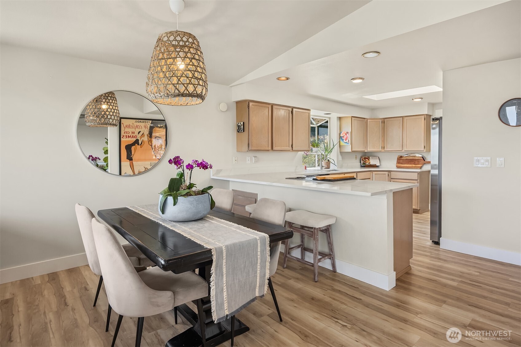 Dining area with a dark table and woven pendant beside a bright kitchen with a white peninsula.