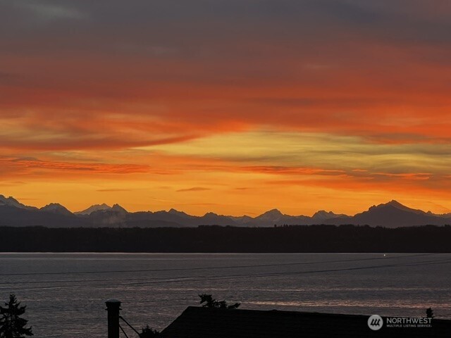 Sunset over the water with a silhouetted mountain range on the horizon.