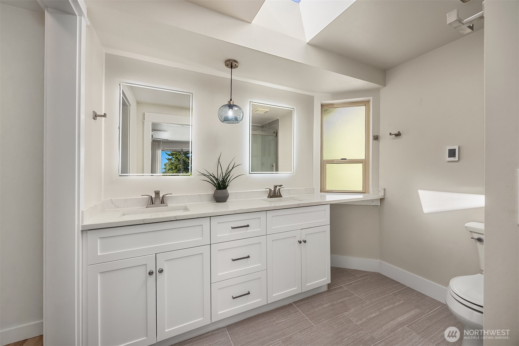 Bathroom with a white double vanity, marble-look counters, and a skylight.