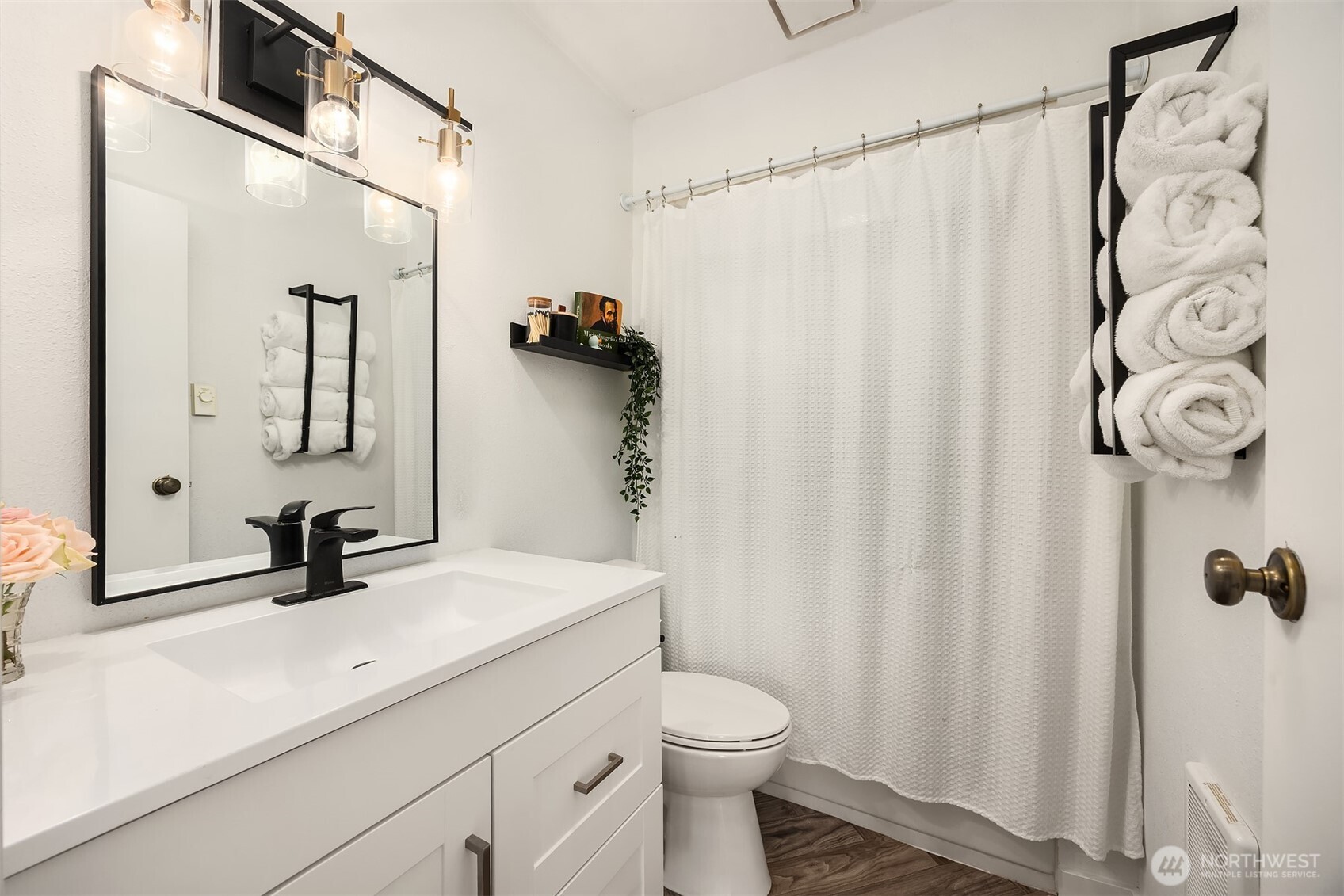 Bright bathroom with a white vanity, black-framed mirror, shower curtain, and wall-mounted towel rack.
