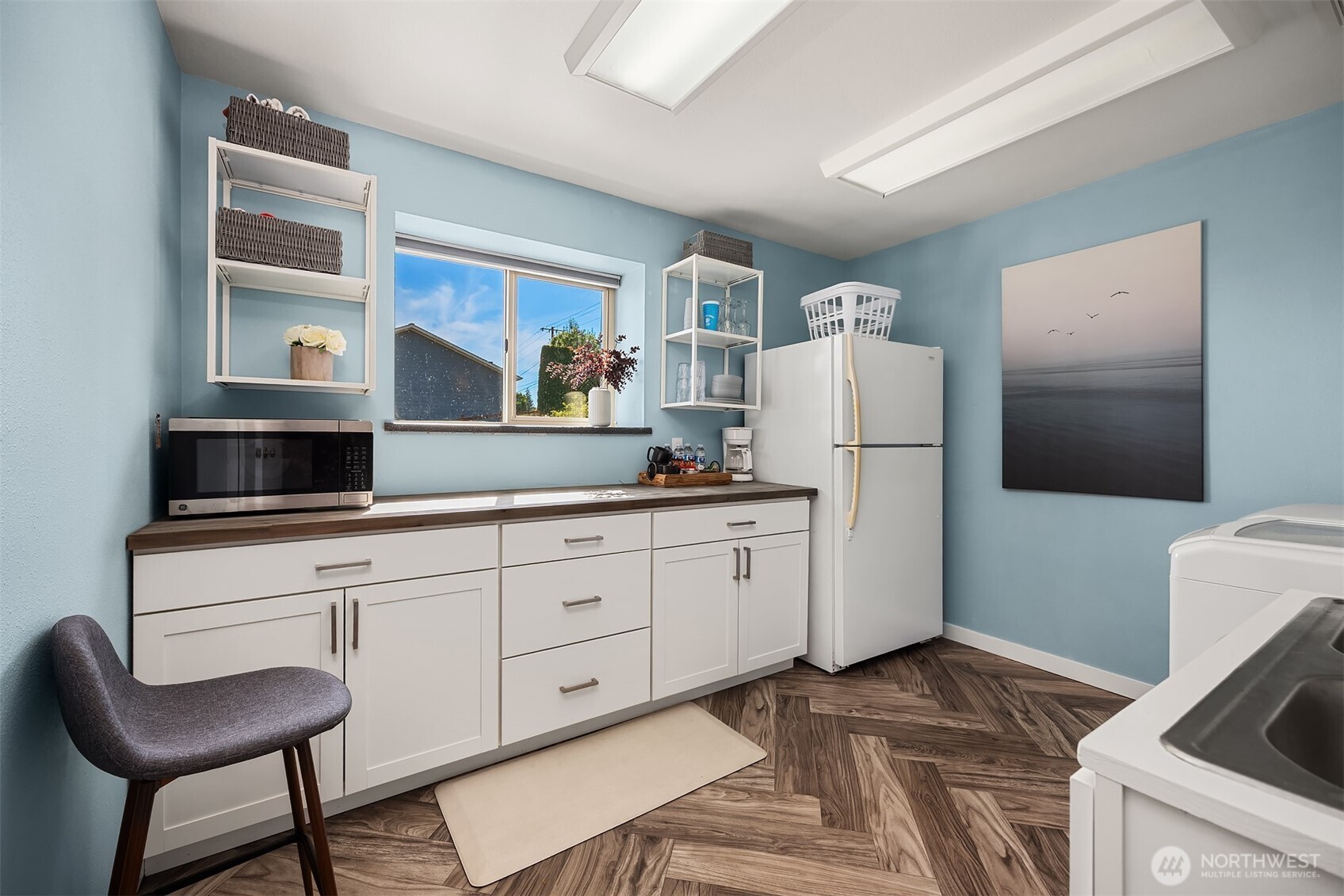 Laundry room with white cabinets, refrigerator, washer and dryer, and blue walls.