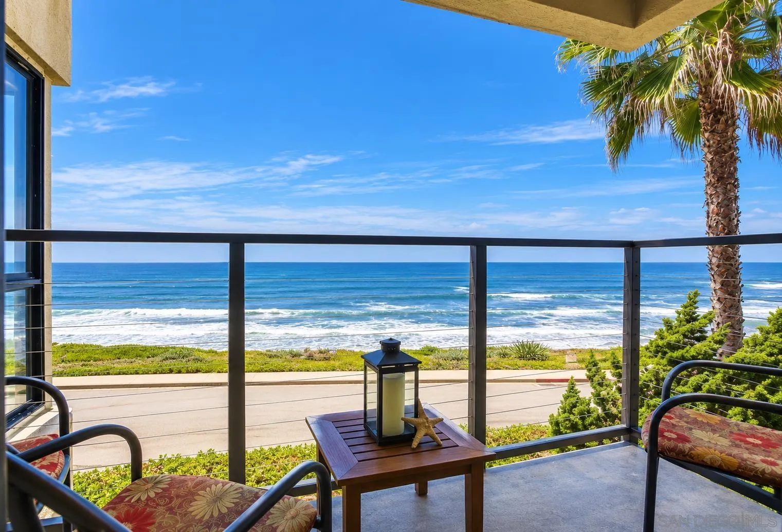 Furnished balcony overlooking the ocean, framed by a palm tree.