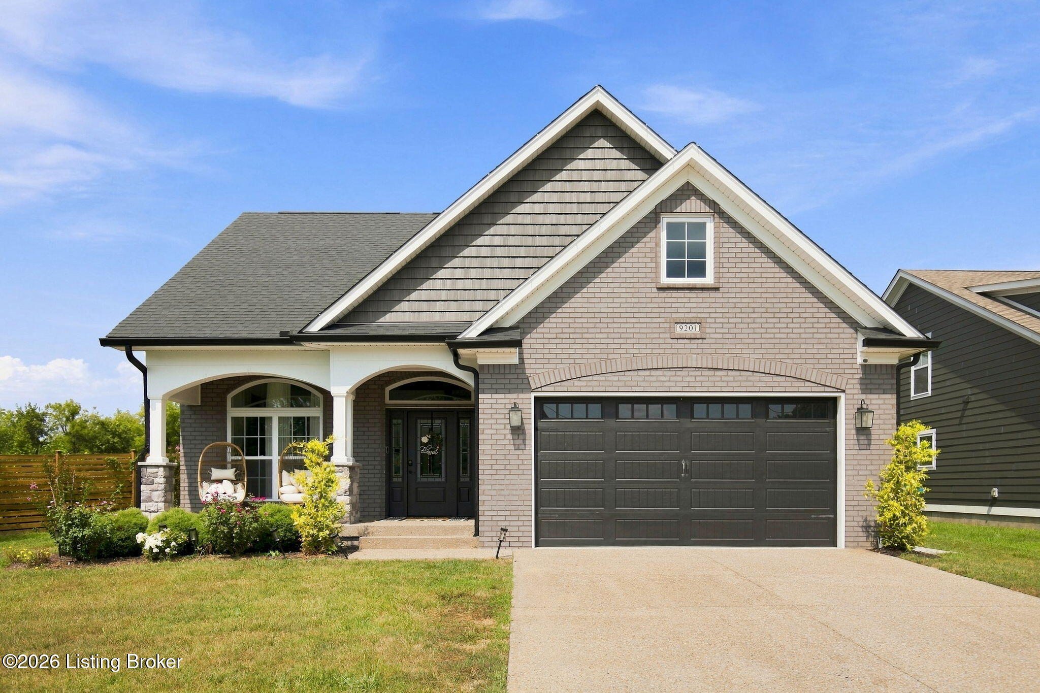 Two-story brick home with steep gables, covered porch, dark double garage door, and landscaped front garden.