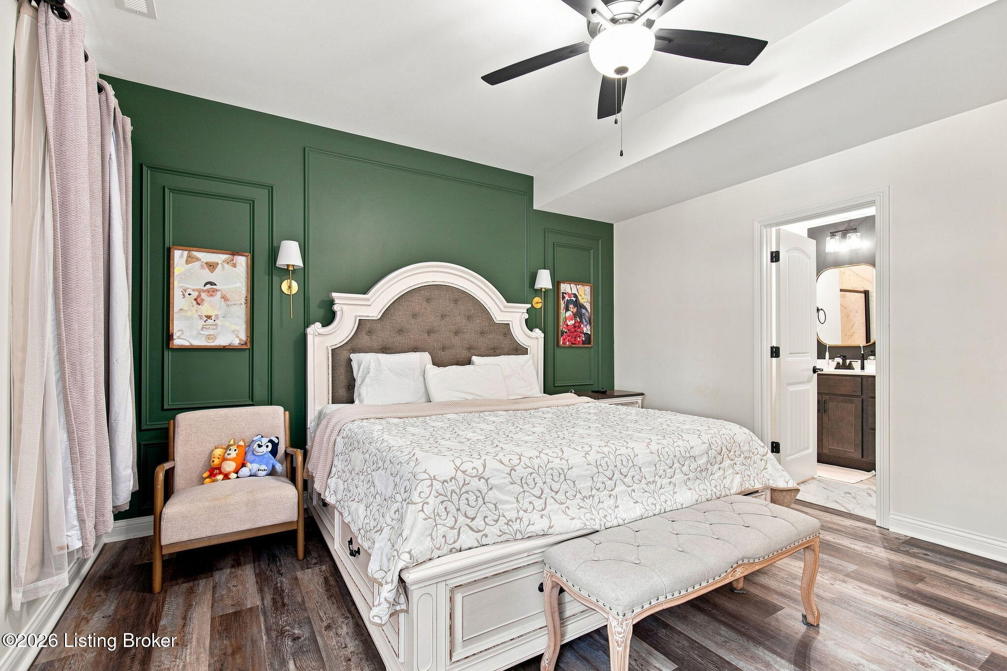 Bedroom with a dark green paneled wall, ornate white bed, upholstered bench, and open ensuite bathroom doorway.