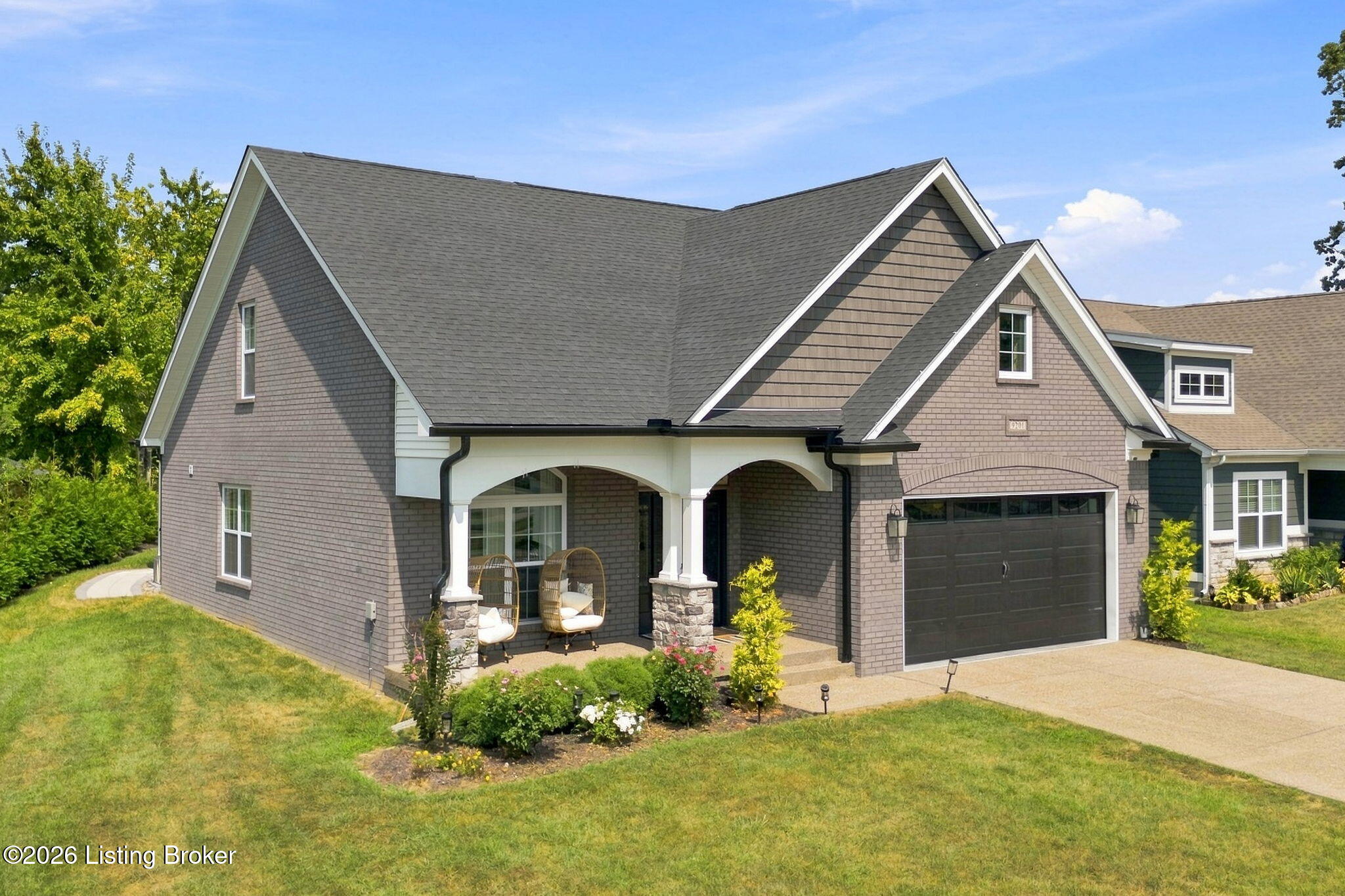 Gray-brown gabled home with a covered porch, hanging chairs, dark double garage, and landscaped front yard.