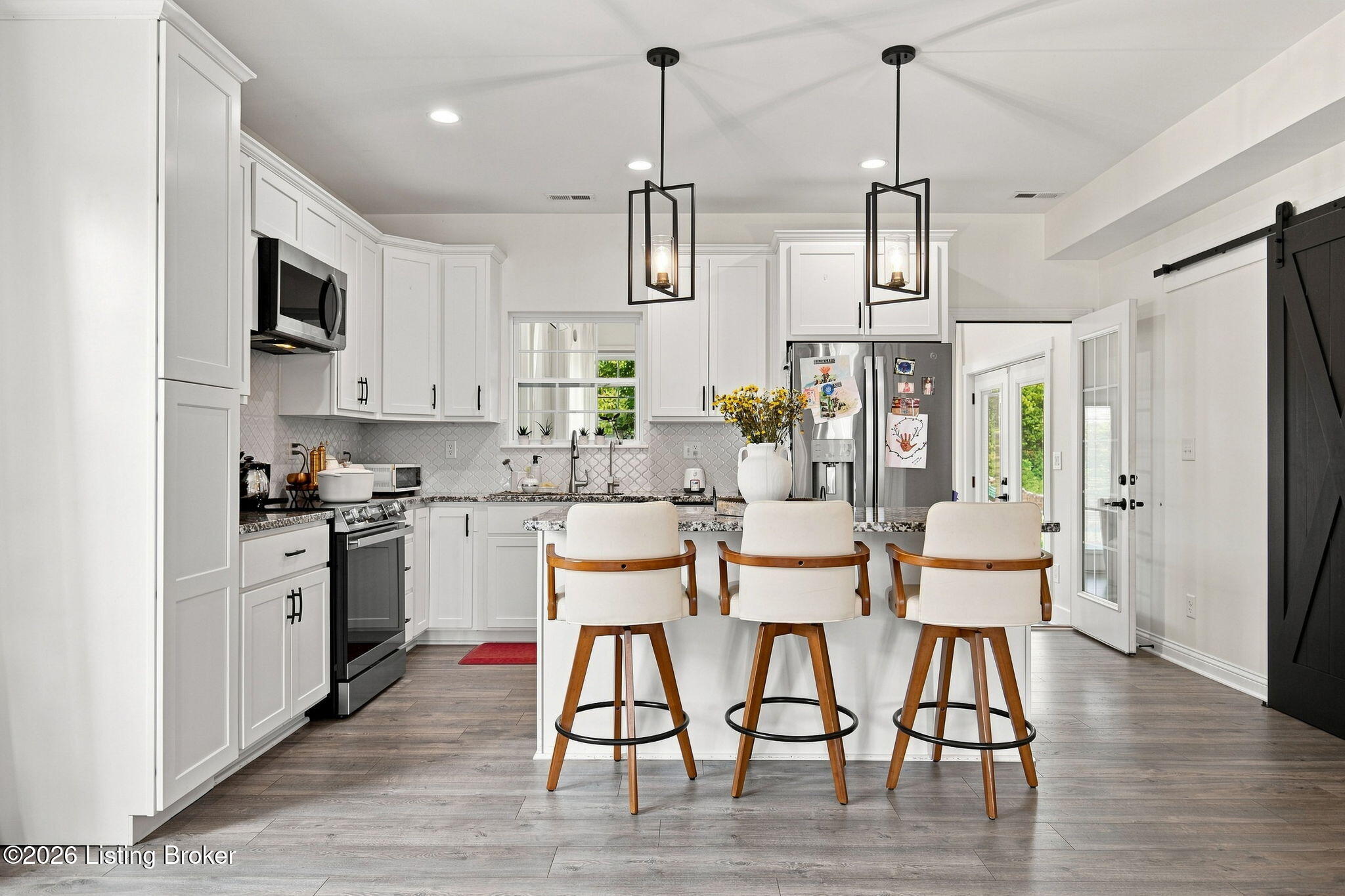 Bright white kitchen with stainless appliances, patterned backsplash, and an island with three wooden stools.