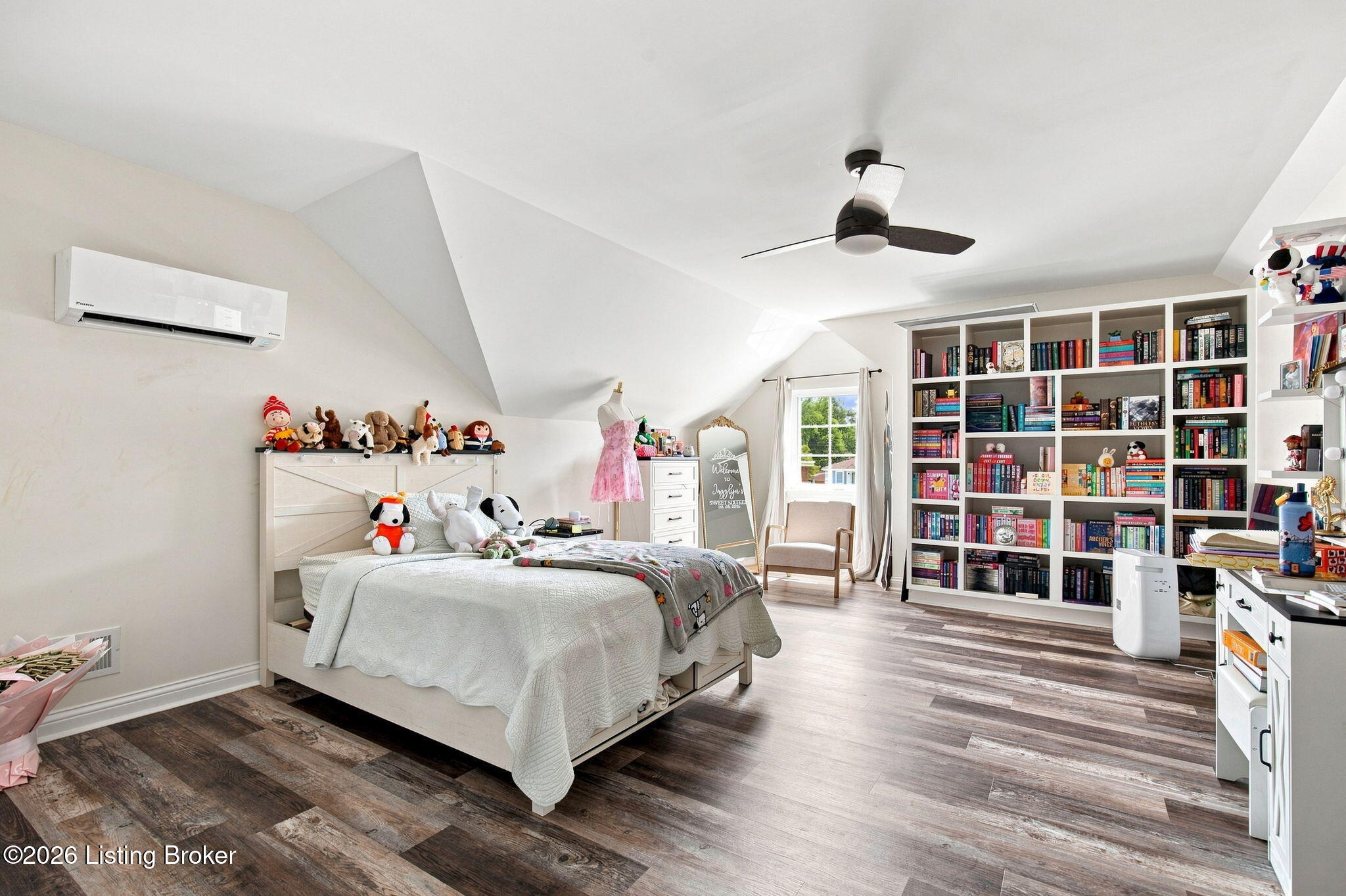 Bedroom with a sloped ceiling, stuffed animals on the bed, and extensive white bookshelves.