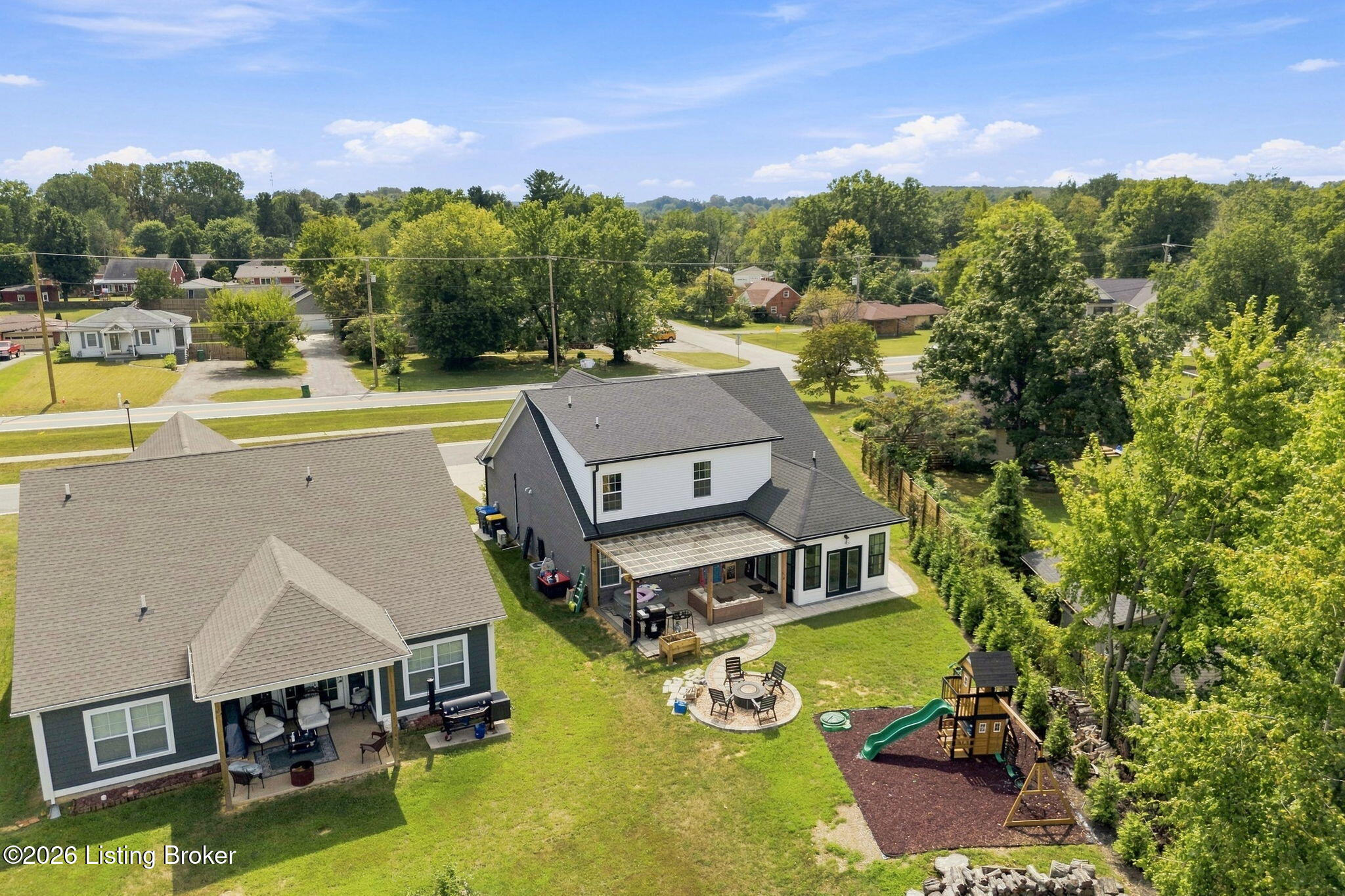 Aerial view of neighboring homes with covered patios, a circular dining area, and a backyard play set.
