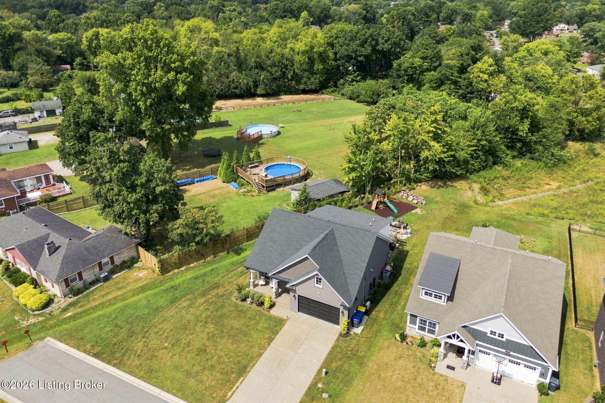 Aerial view of a home and expansive fenced backyard with two pools and wooded surroundings.