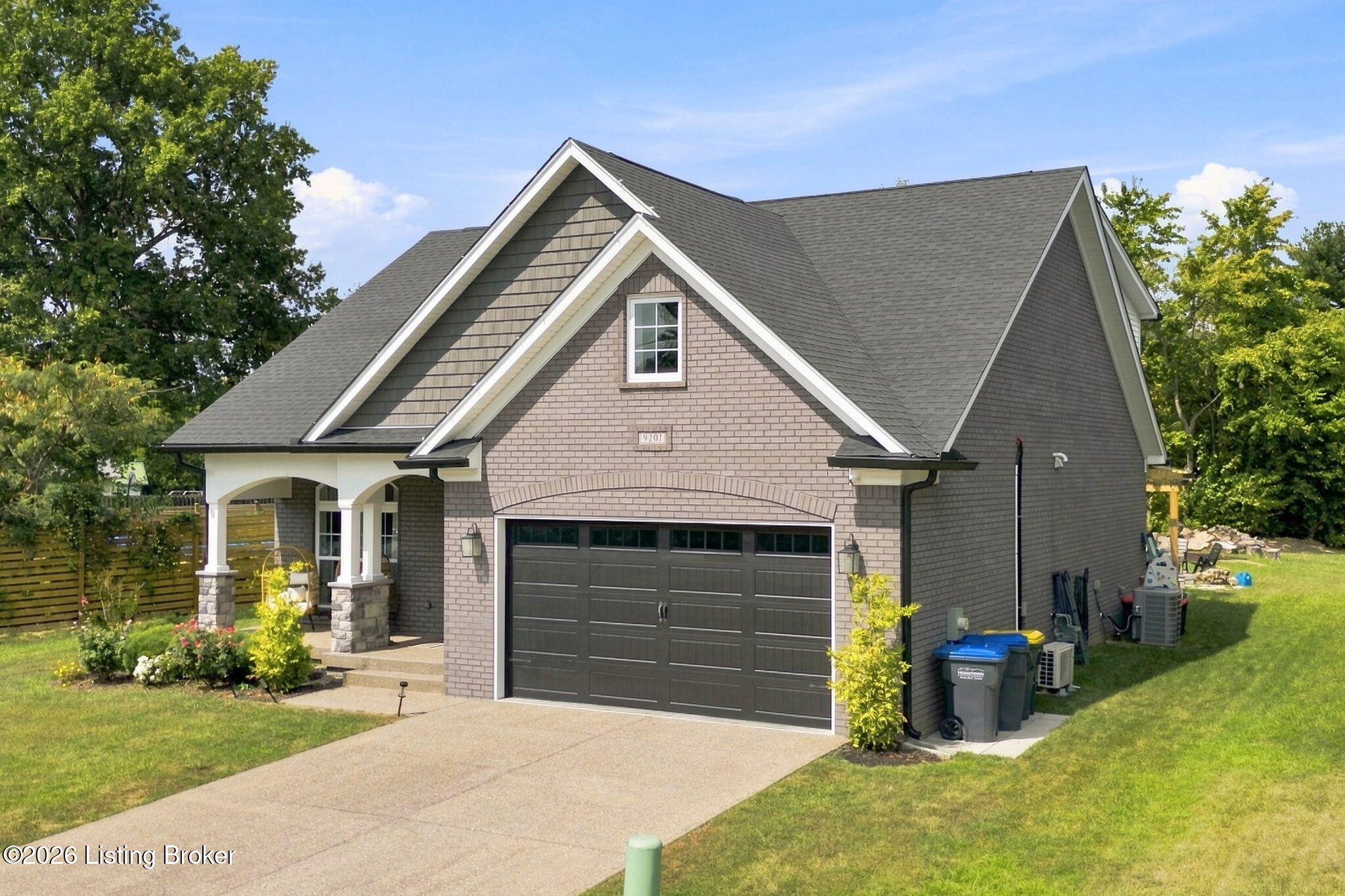 Gray-brick home with steep gables, a covered porch, and a dark double garage door.