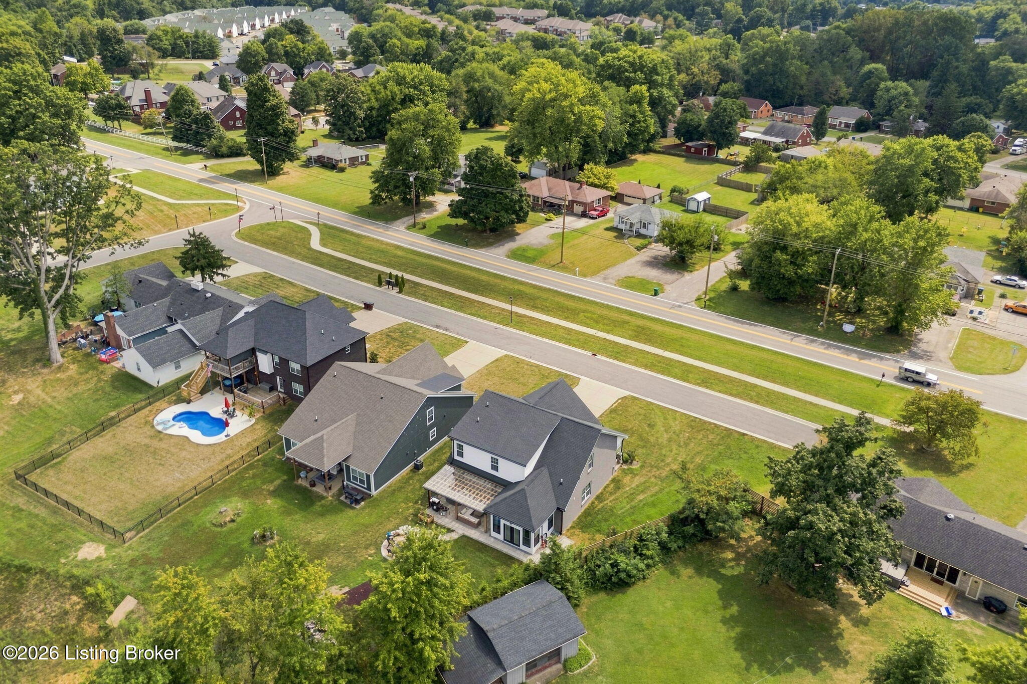 Aerial view of homes and tree-lined streets, with a fenced backyard pool.