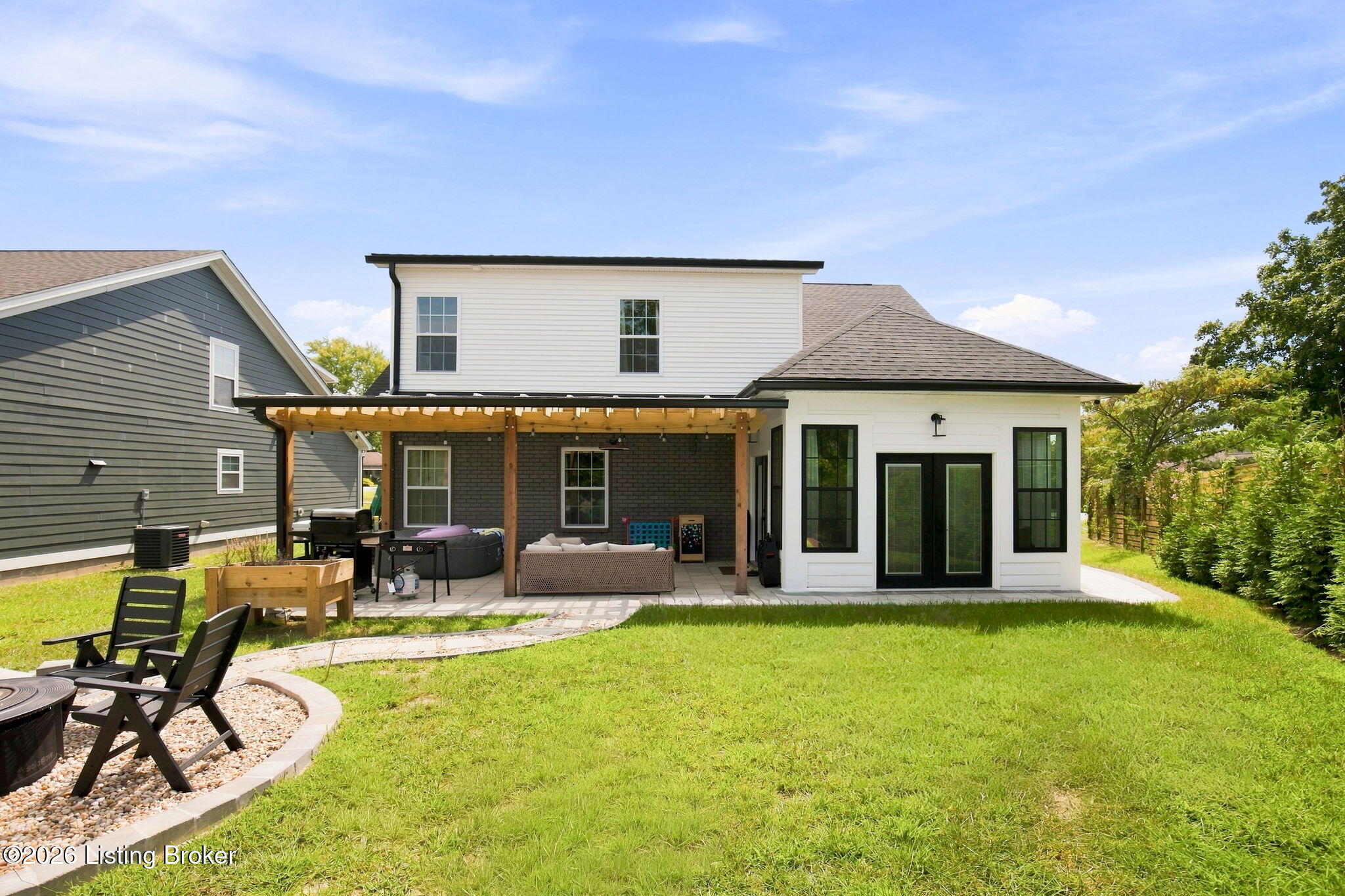 White two-story home with a covered pergola patio, outdoor seating, and a broad green backyard.